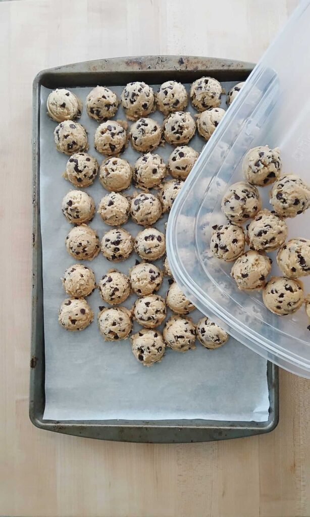Moving cold chocolate chip cookie dough portions from a tray into a container for the 48-hour chill.