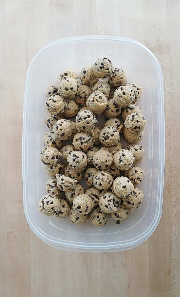 A clear airtight container filled with layers of mini chip cookie dough balls, ready to be refrigerated for a 48 hours