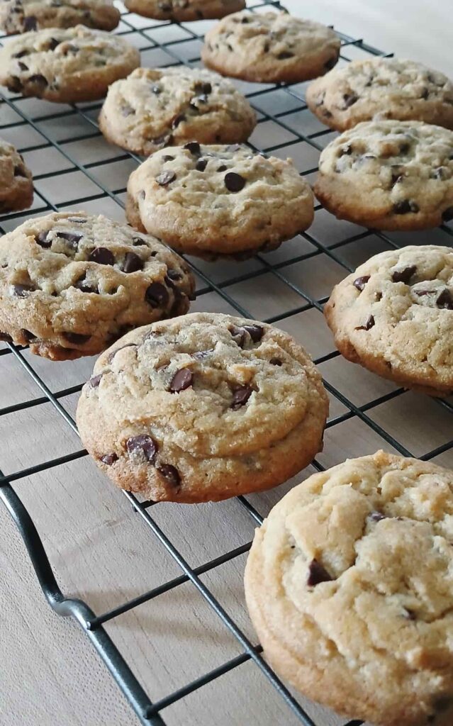 A wire cooling rack filled with freshly baked, light golden-brown mini chip cookies, showing their soft centers and slightly cracked, chewy tops.