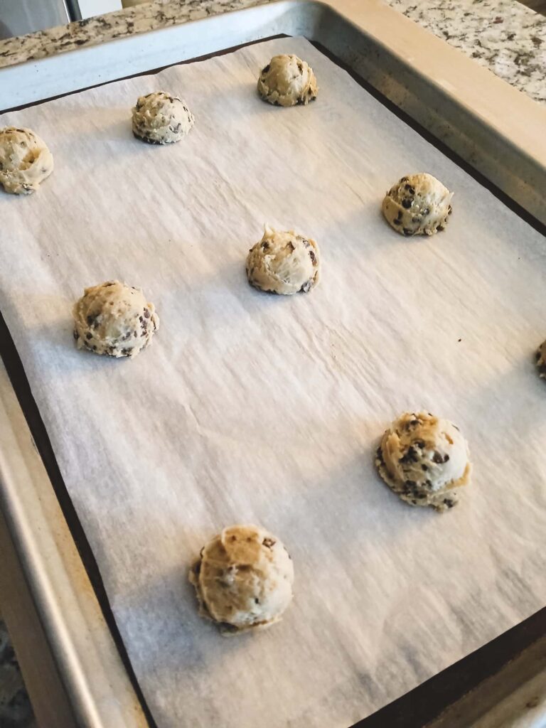 Chilled chocolate chip cookie dough balls neatly spaced on a large parchment-lined baking sheet, ready to bake