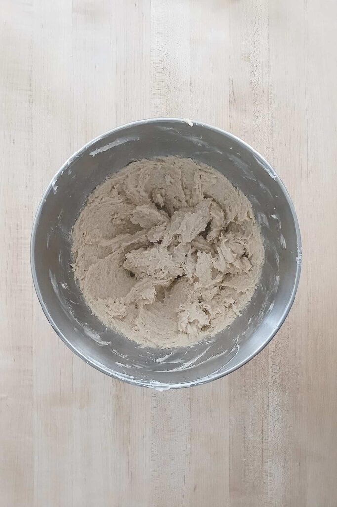 A mixing bowl of cookie dough base after creaming in the light brown sugar, showing a smooth and slightly pale brown mixture.