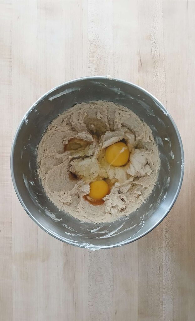 Two whole egg yolks resting on top of a fluffy, light brown creamed sugar and fat mixture before being emulsified.
