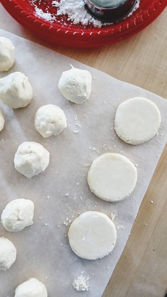 Gently flattening shortbread cookie dough balls with a measuring cup before baking