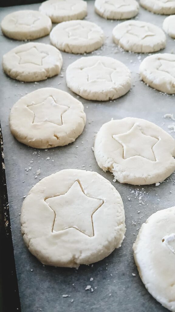 Close-up of flattened whipped shortbread cookies with a distinct star shape imprint in the center of each, on a pale, snowy white dough.