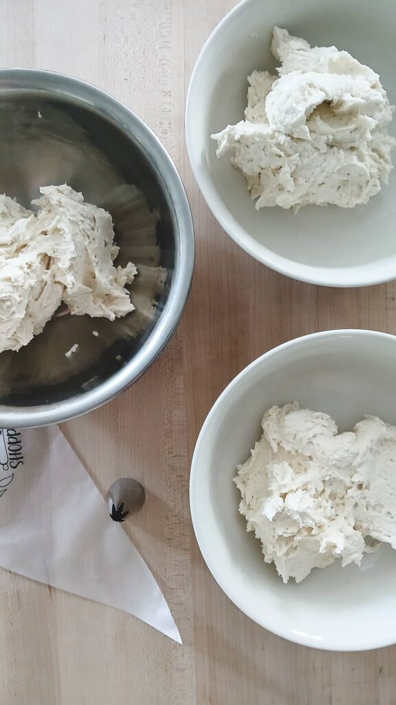 Three bowls of whipped shortbread dough with about to be colored with food coloring and a piping bag with a star tip ready for shaping.