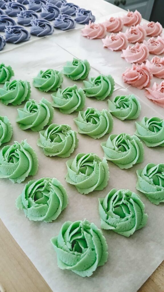 Piped pastel-colored shortbread rosettes on a baking sheet, showing the detailed ridges before being placed in the freezer to chill.