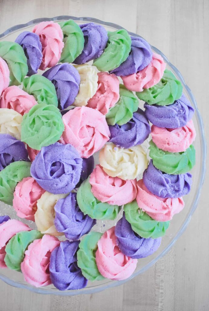 Overhead view of a serving tray filled with pastel purple, pink, and green whipped shortbread rosettes, showing how the piped dough holds its detailed shape after baking.