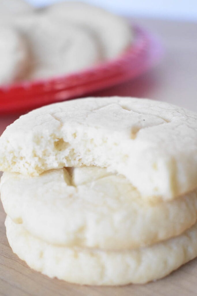 Close-up of a stack of three buttery whipped shortbread cookies, highlighting the melt-in-your-mouth, delicate crumb of the top cookie after a bite.