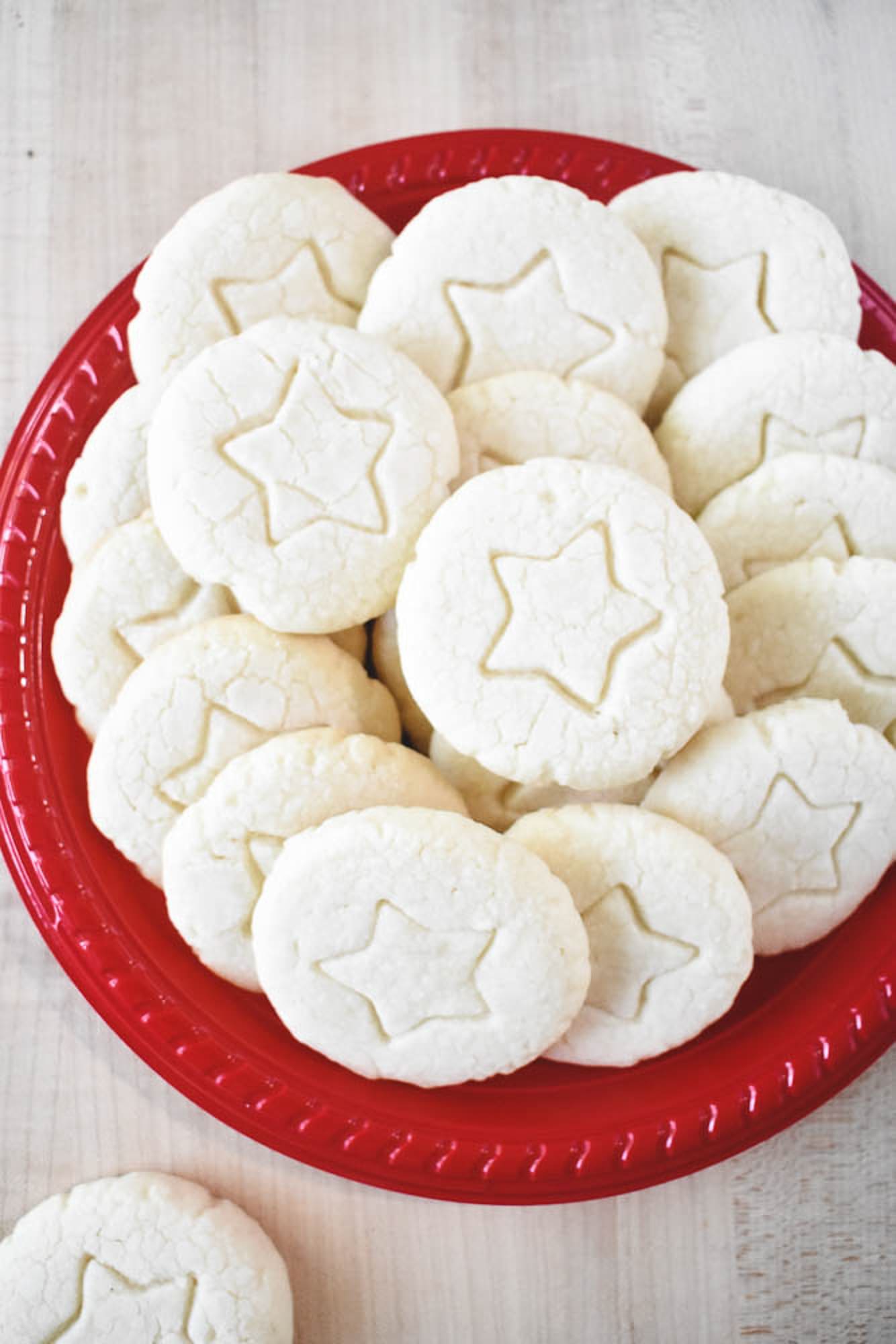 A red plate piled with round, pale whipped shortbread cookies featuring a delicate star imprint in the center of each.