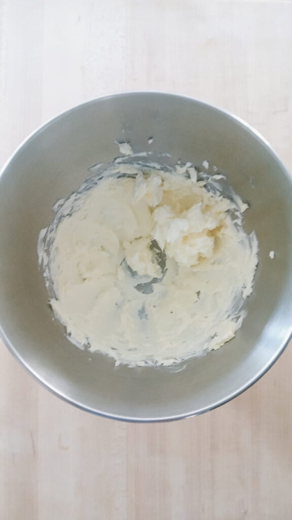 A metal mixing bowl showing softened butter after one minute of whipping until creamy and smooth before adding powdered sugar.