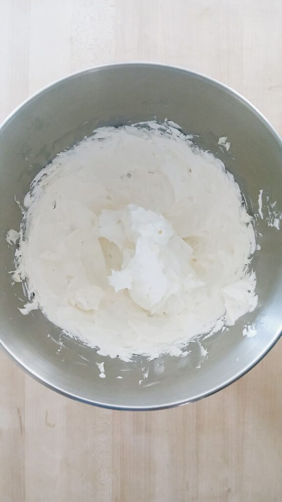 A stand mixer bowl filled with the whipped shortbread base after ten minutes, showing a pale, snowy white, and high-volume mixture that looks light and airy.
