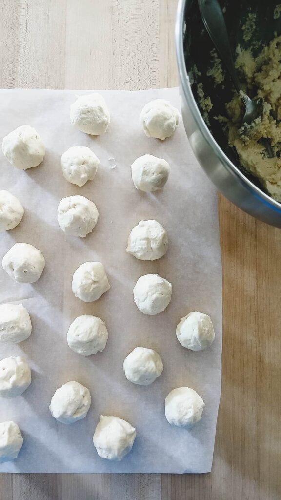 Measured portions of whipped shortbread cookie dough on a parchment-lined baking sheet, prepared for hand-rolling into balls.